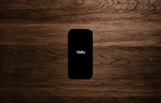 Schwarzes Smartphone auf Holzhintergrund mit HELLO auf dem Bildschirm in weisser Schriftfarbe